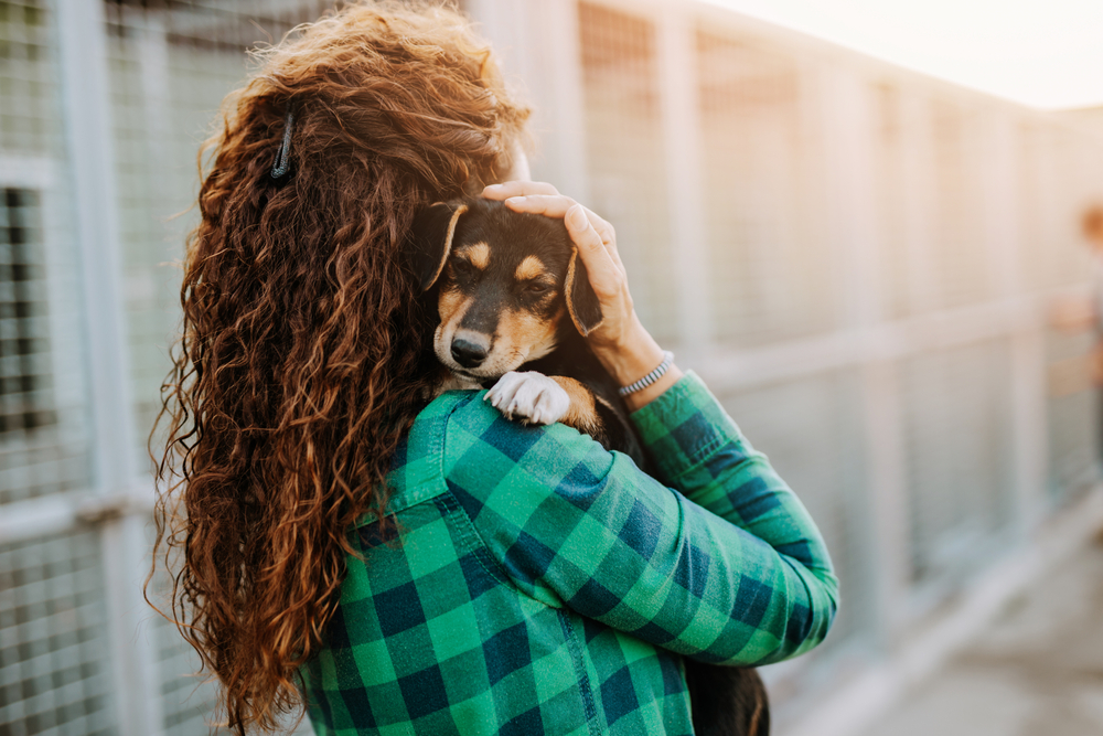 A woman embraces a rescue dog lovingly outside an animal shelter, capturing a tender moment of trust and care.